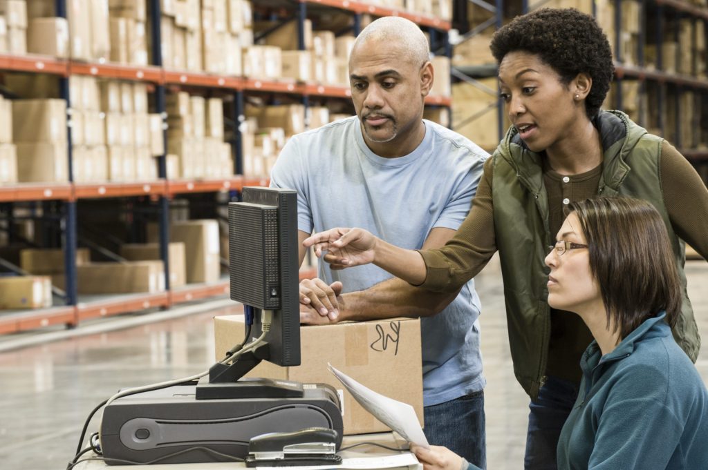 Warehouse workers checking inventory on a computer in a large distrubiton warehouse.